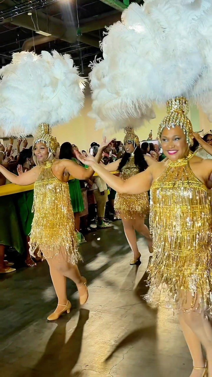 Women in gold sequined dresses and white feathered headpieces dancing at a party.
