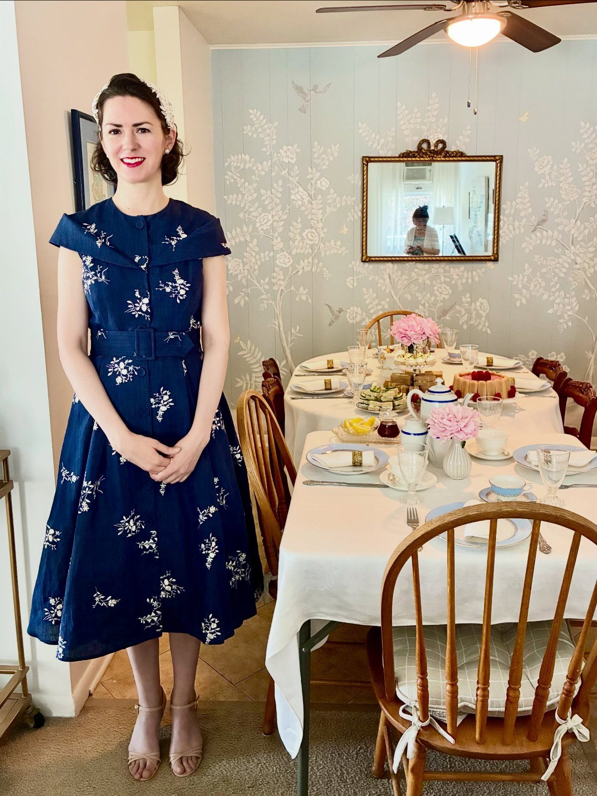Woman in floral dress standing by a table set for a tea party.