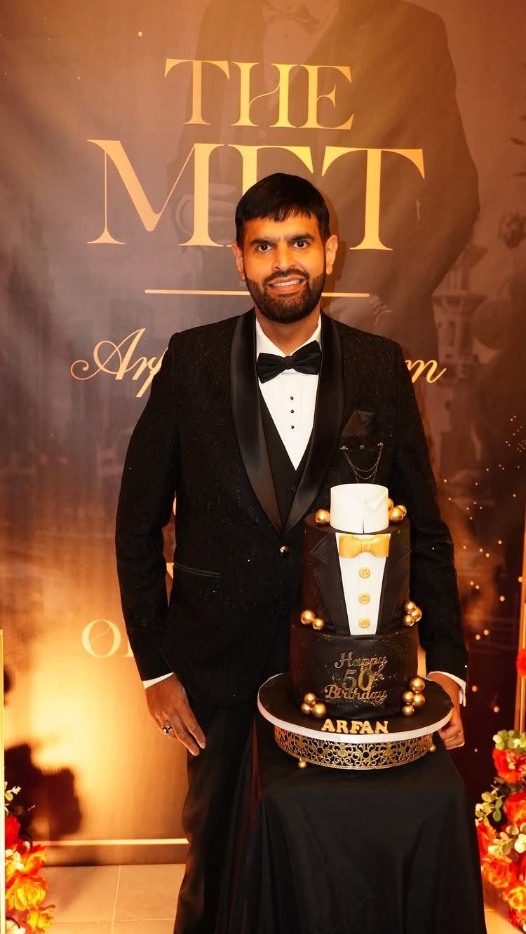Man in a tuxedo standing beside a tuxedo-themed 50th birthday cake.
