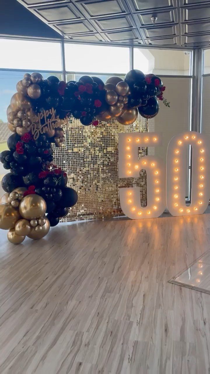 Gold sequin backdrop with black and gold balloon arch and lit 50 numbers.