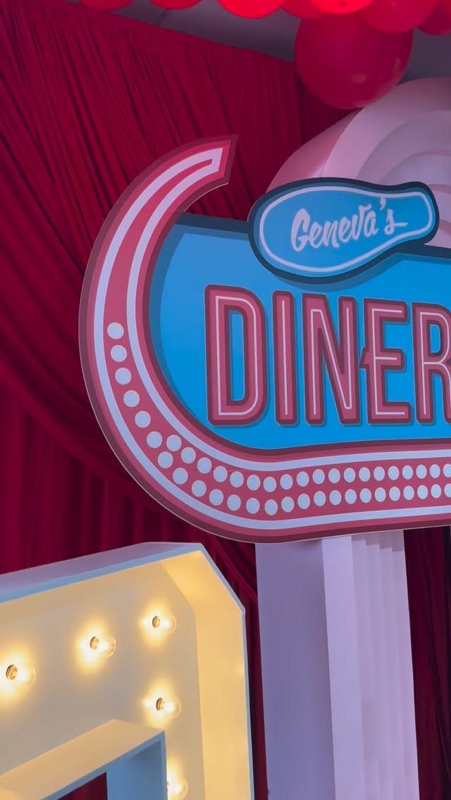 Retro diner sign with pink and blue colors against a red curtain backdrop.