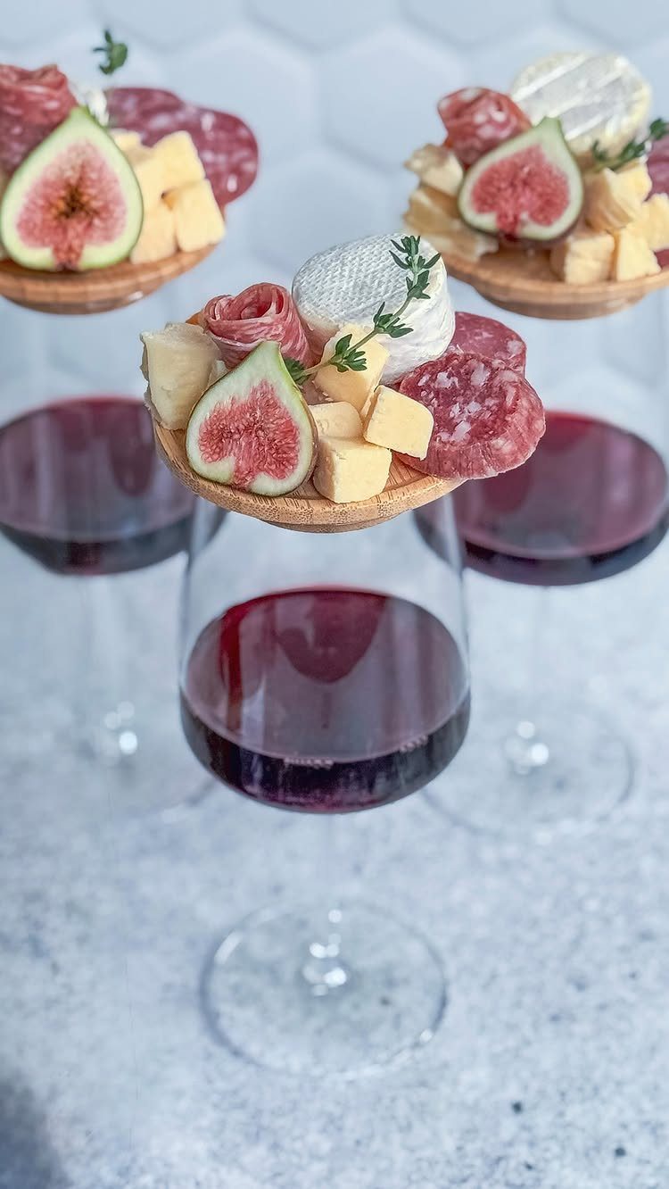 Red wine glasses topped with crackers, cheese, salami, and fresh fig slices.