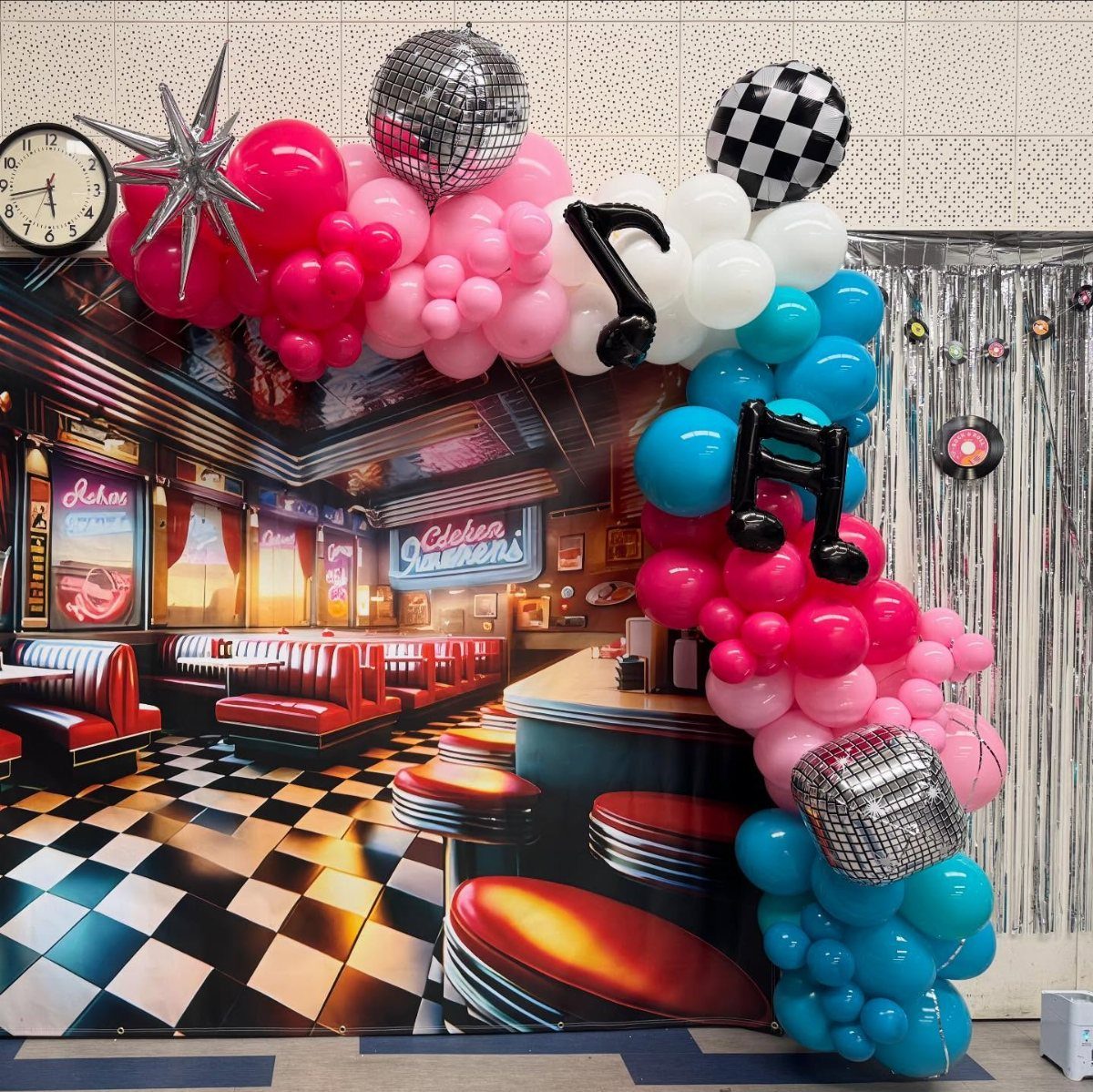 Pink, white, and aqua balloon garland framing a retro 1950s diner backdrop.