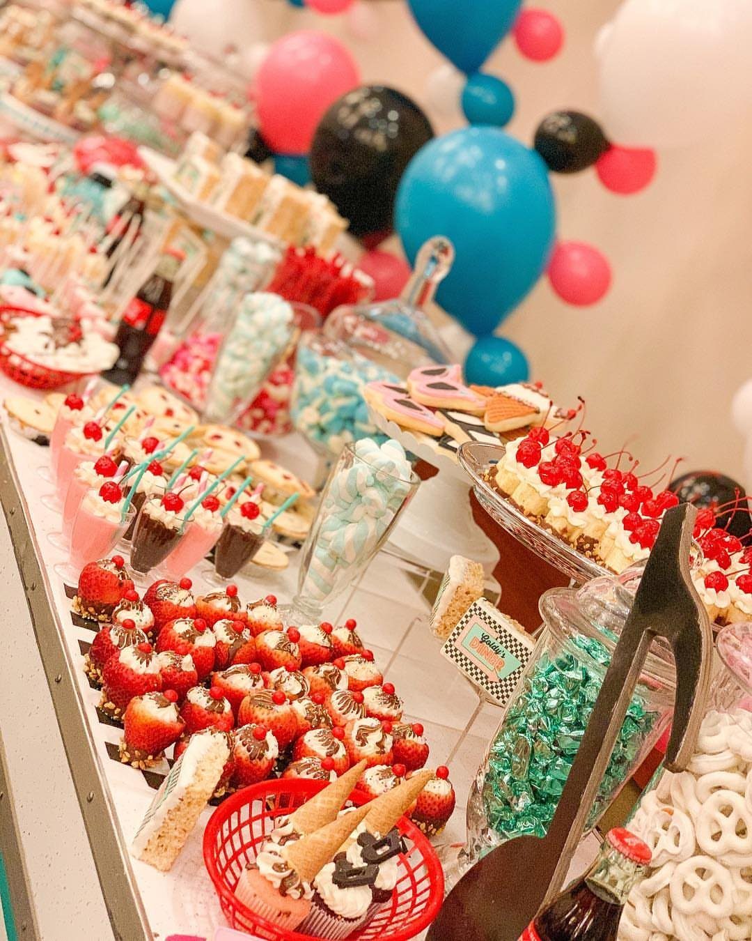 Dessert table with chocolate strawberries and blue candies with colorful balloons behind.