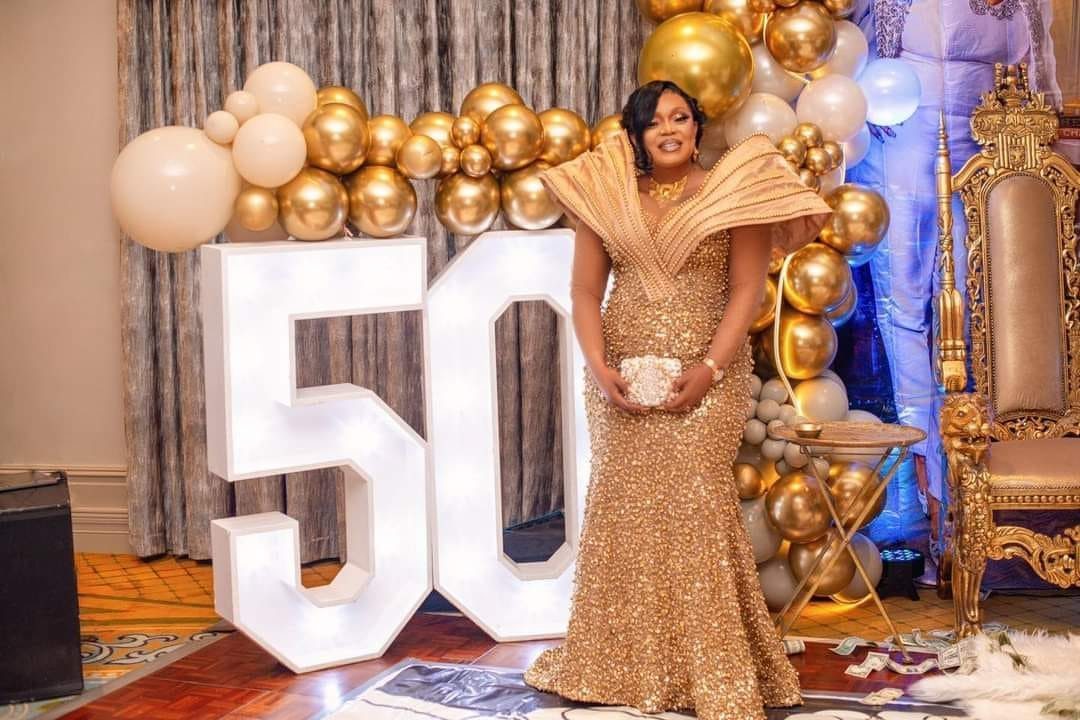 Woman in a gold sequined gown posing by large glowing 50 birthday numbers