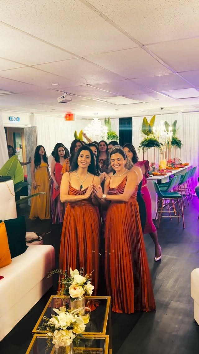 Women wearing long rust-colored pleated dresses posing in a decorated party room.