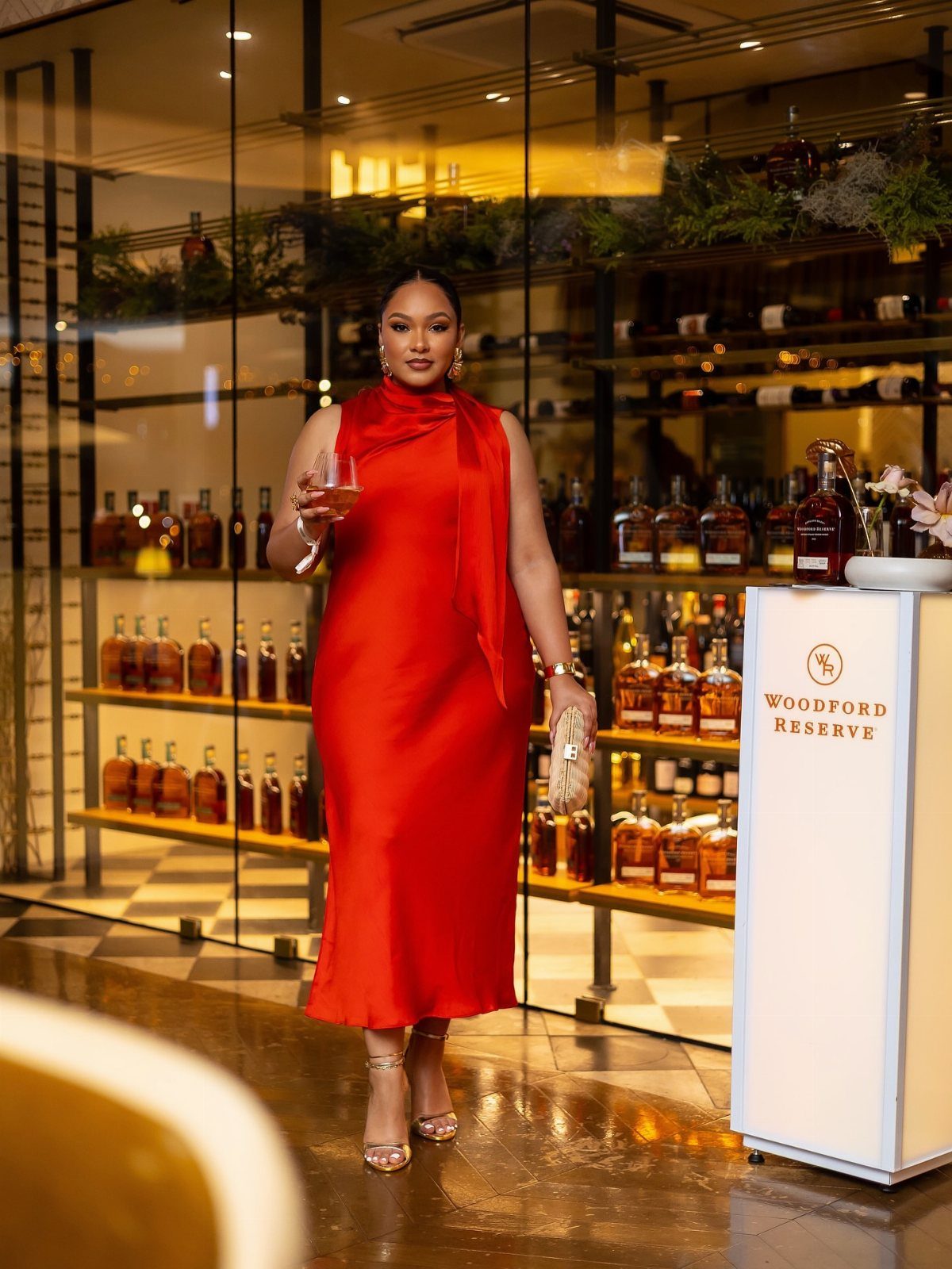 Woman in a red satin midi dress holding wine in a bar setting