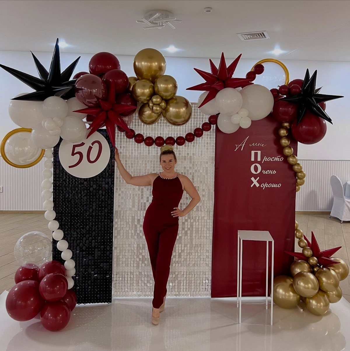 Woman in a sleek red jumpsuit posing by a 50th birthday balloon backdrop