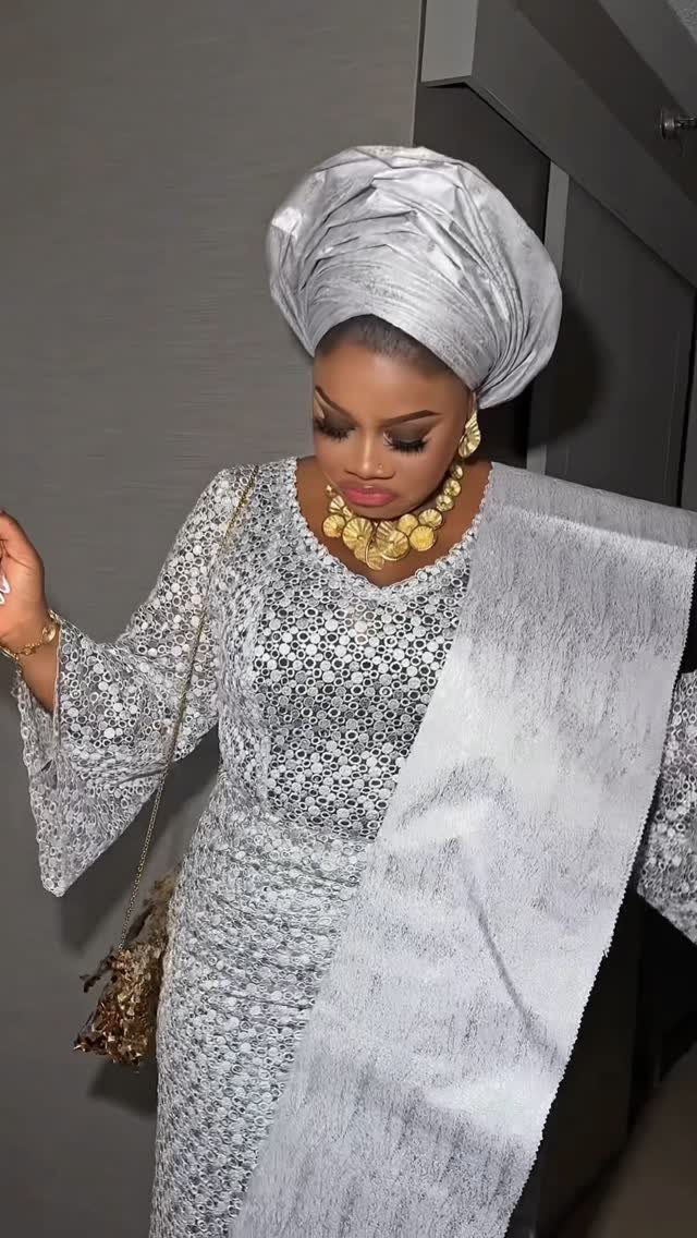 Woman in a silver patterned dress and headwrap wearing chunky gold jewelry.