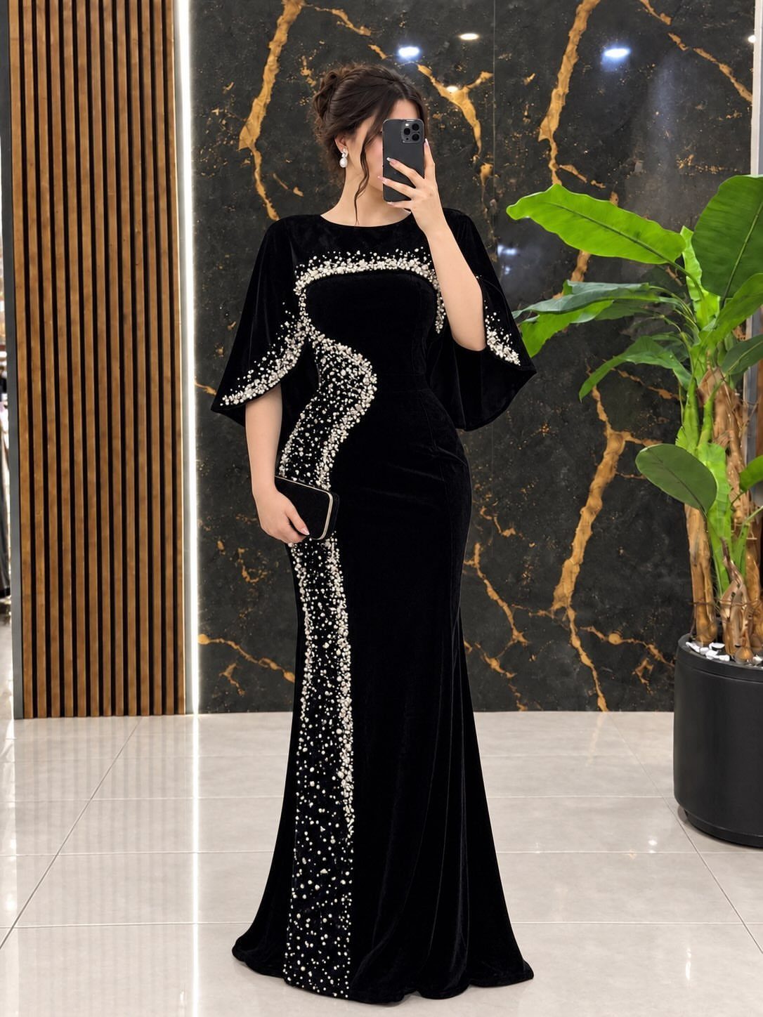 Woman in a black velvet cape-sleeve formal gown with silver rhinestone detailing.