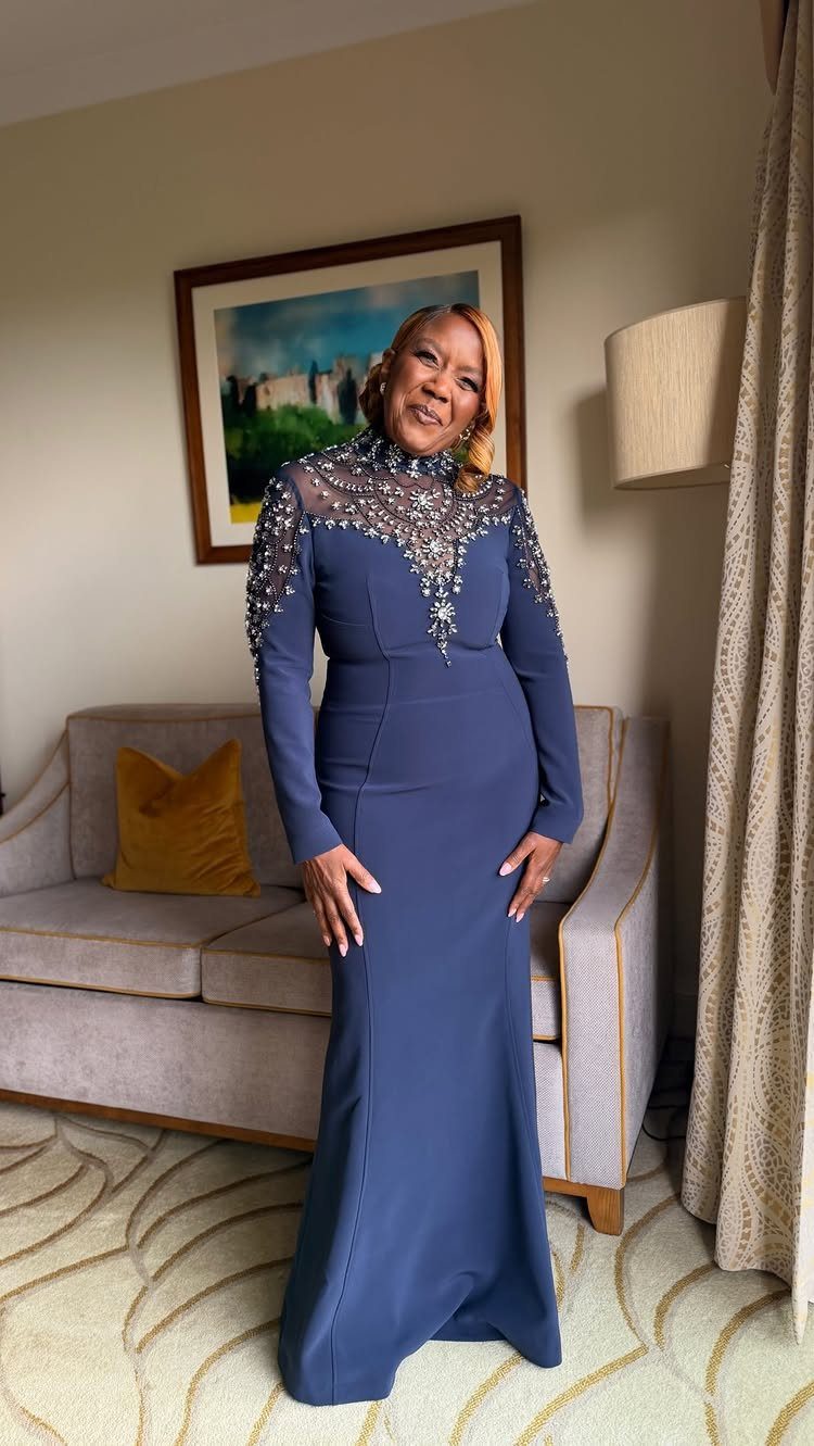 Woman in a navy blue floor-length gown with beaded embellishments on the neckline.