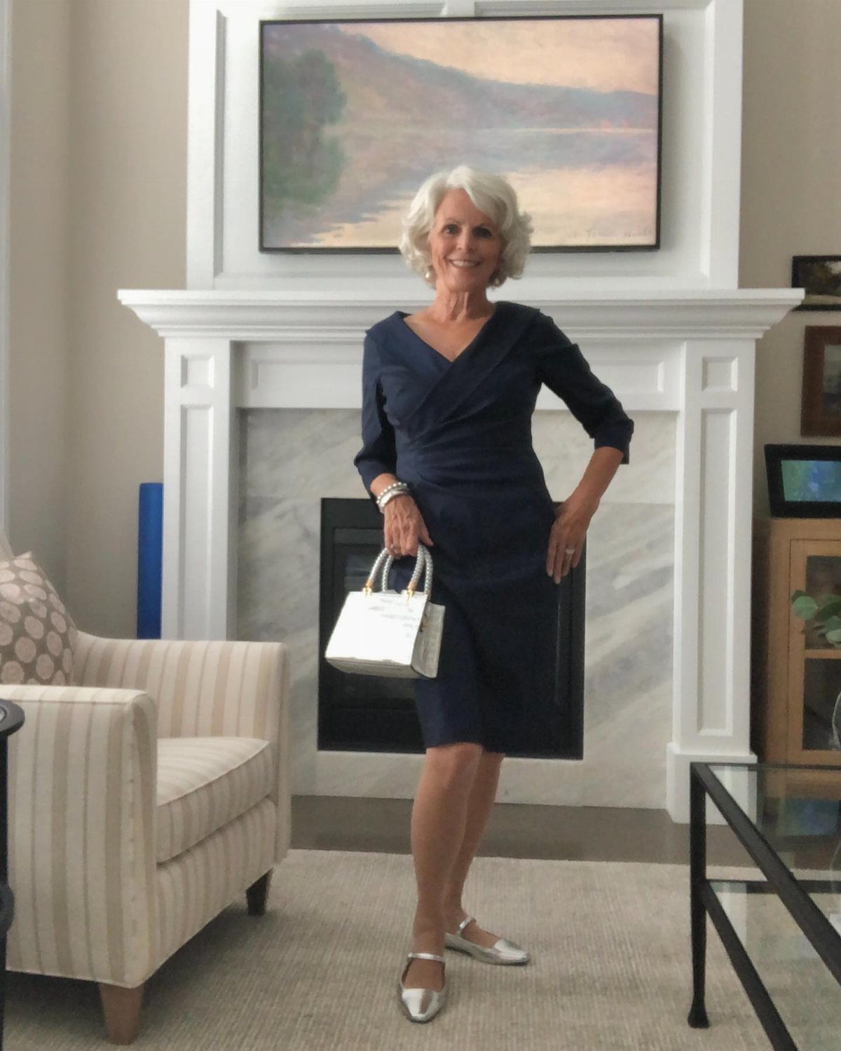 Mature woman wearing a navy blue wrap midi dress and silver pointed-toe flats.