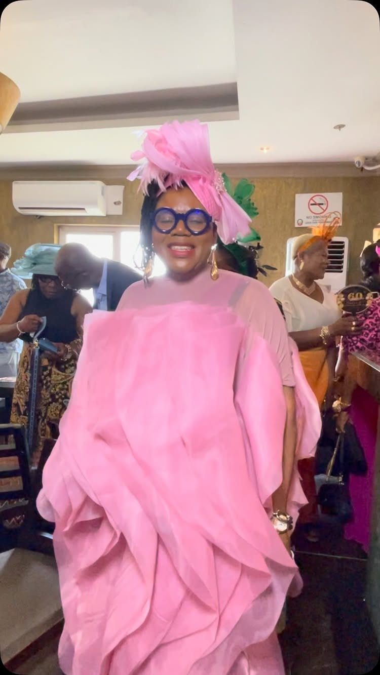 Woman in a voluminous ruffled pink gown and matching headpiece smiling indoors.