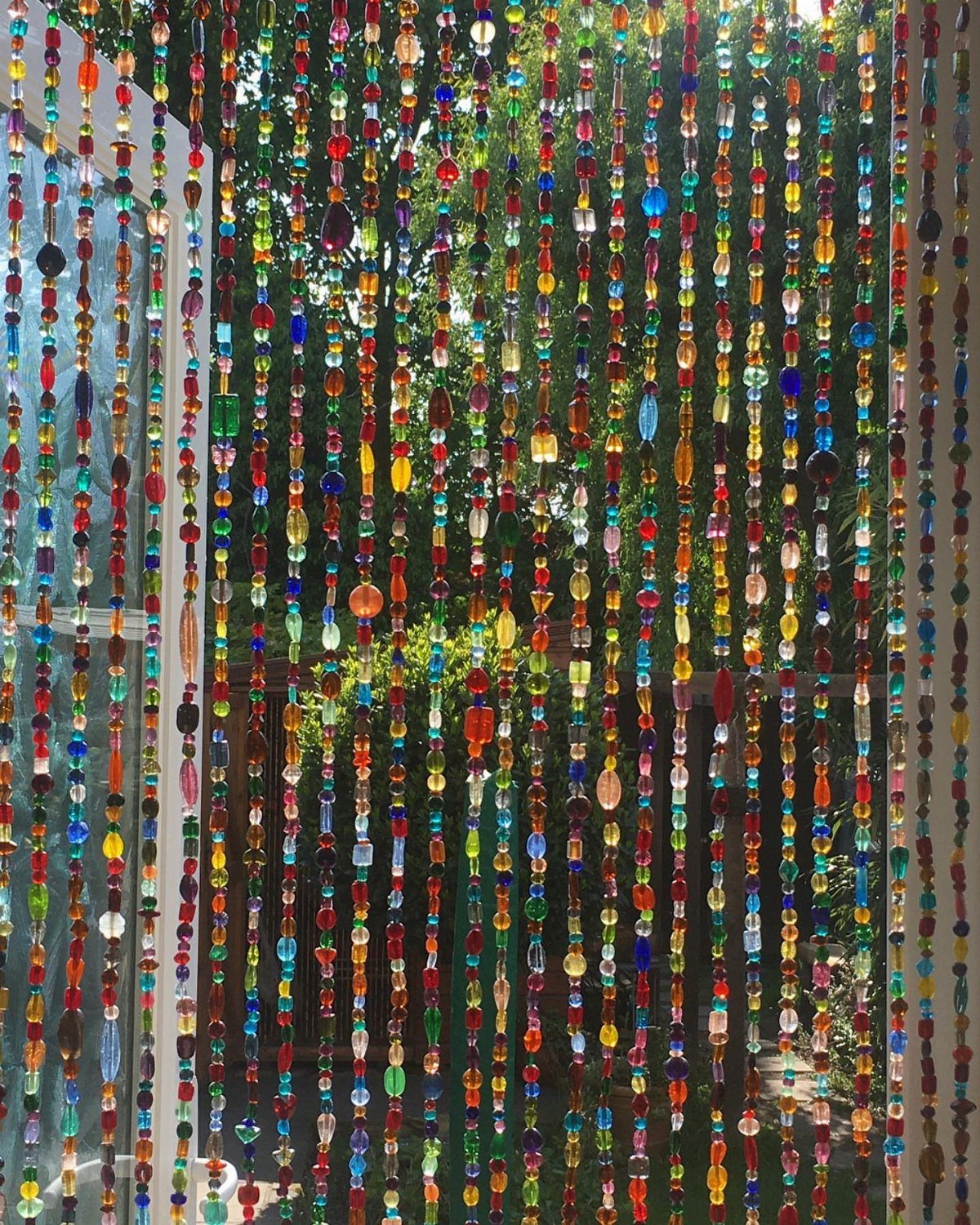 Multicolored glass beaded curtains hanging in a doorway with natural light.