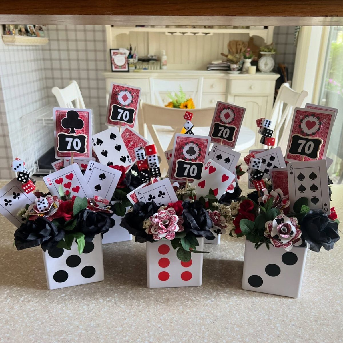 Red and black flowers in dice-themed vases with playing cards for a 70th birthday.
