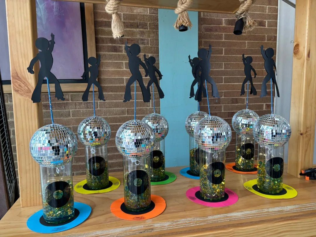 Disco ball centerpieces with dancing silhouettes and miniature records on a wooden table