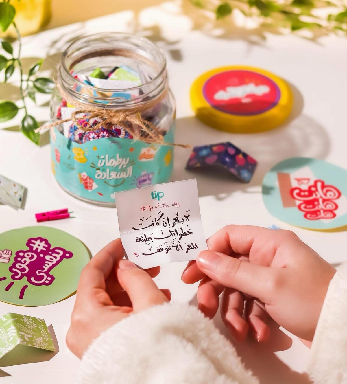 Hands holding a small note from a decorated jar filled with colorful messages.