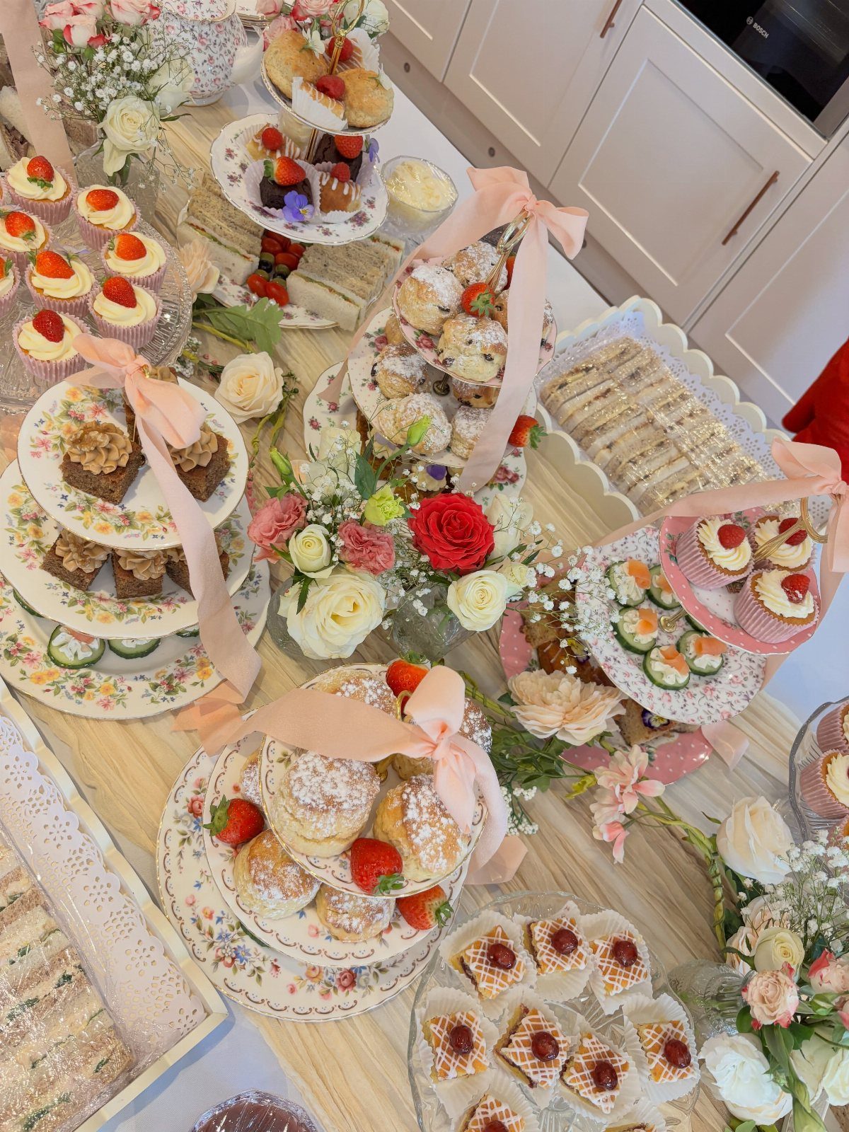 Dessert spread with tiered floral platters, cream puffs, cupcakes, and fresh red roses.