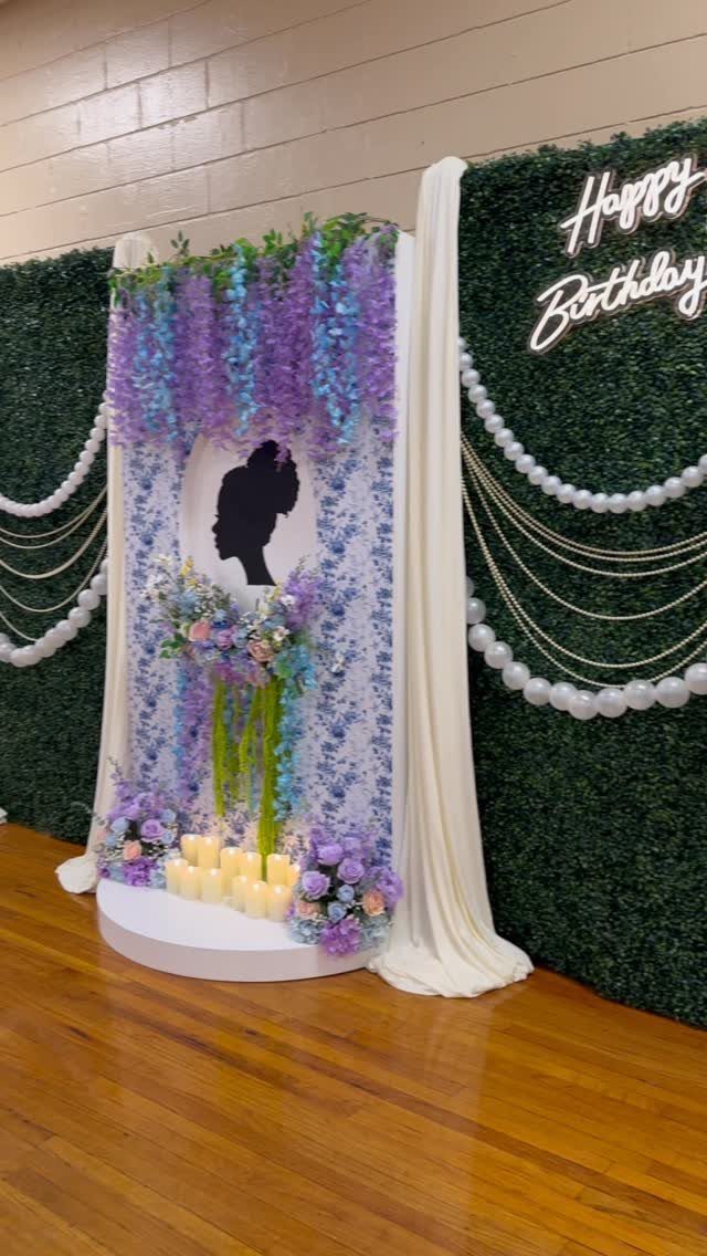 Birthday party backdrop with green hedge wall, purple flowers, and silhouette profile.