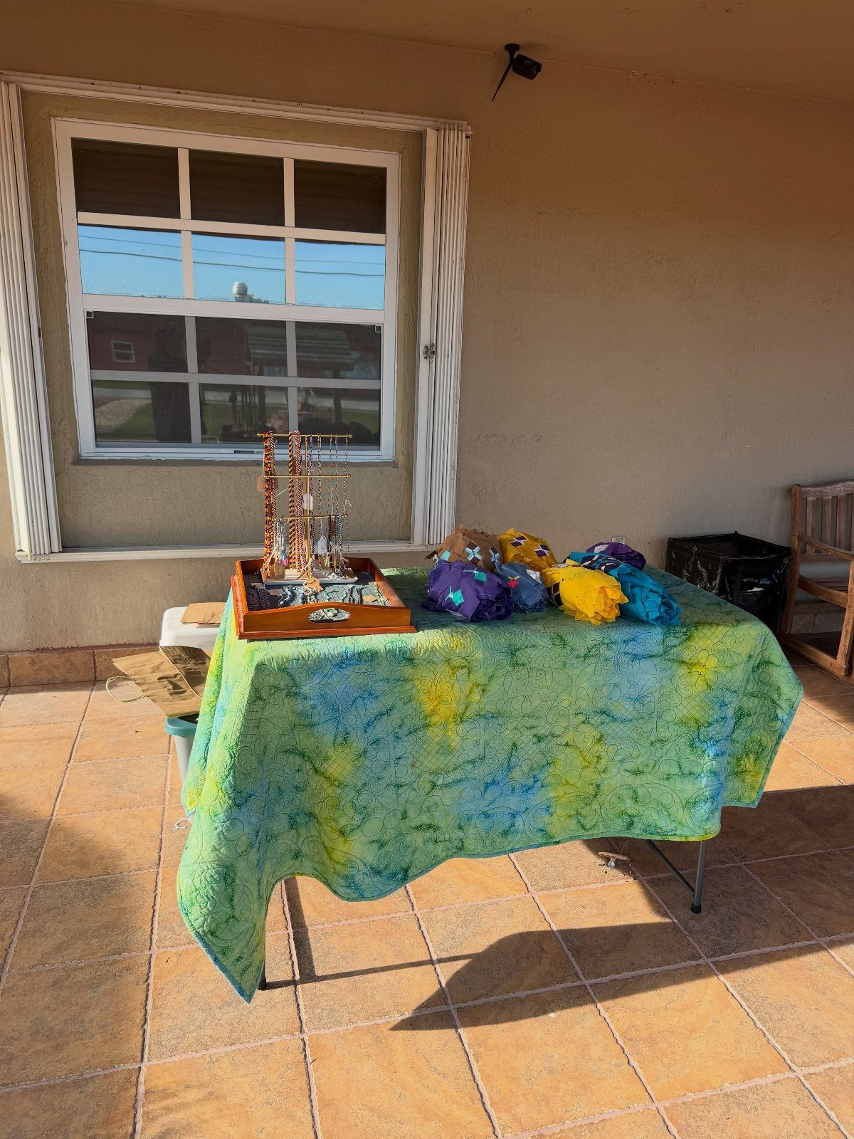 Tie-dyed tablecloth in green, yellow, and blue covering a table on a patio.