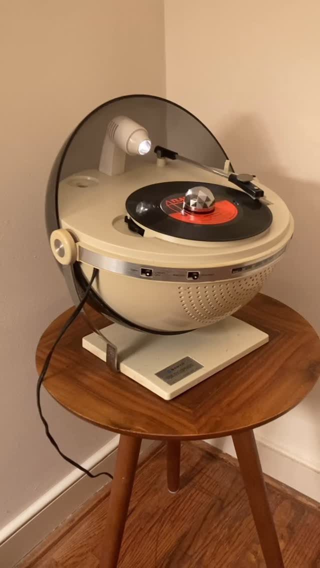 Vintage spherical record player on a wooden table with a small disco ball.