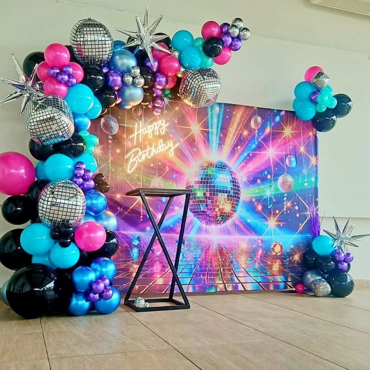 Disco party decor with colorful balloons, silver disco balls, and a neon backdrop.