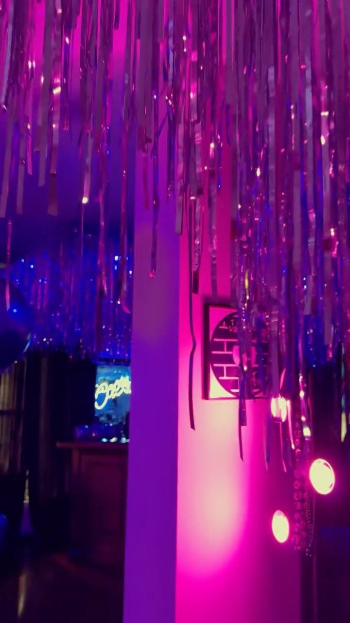 Silver foil fringe curtains glowing under pink and purple neon party lights.
