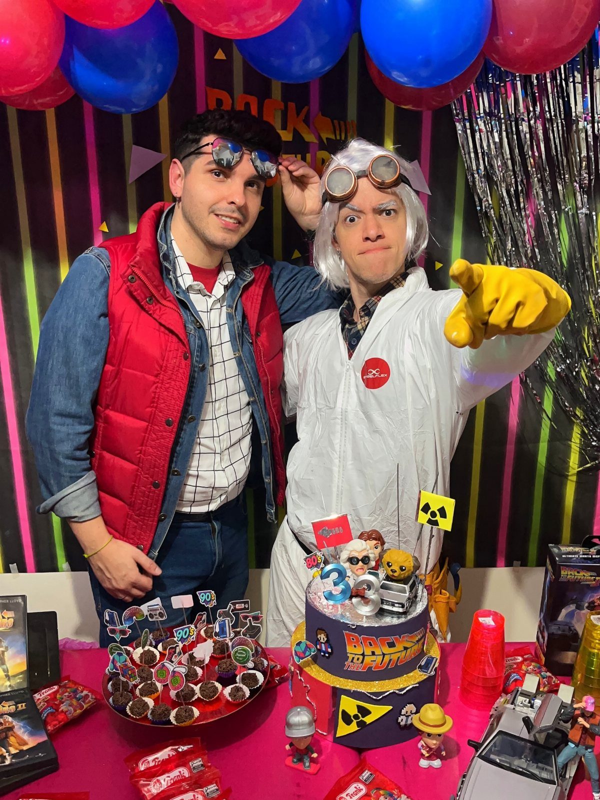 Two men in Back to the Future costumes standing behind a themed party table.
