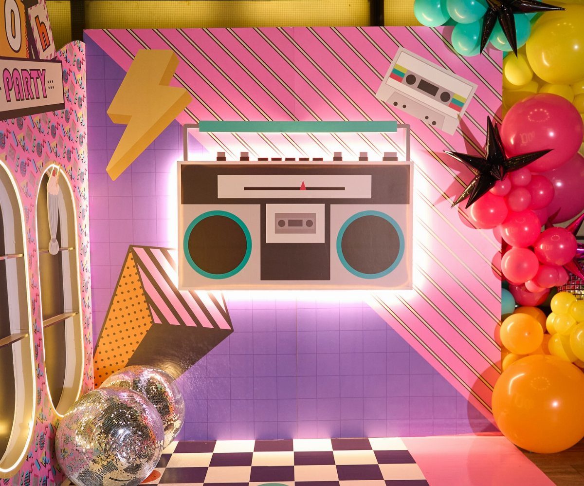 80s party backdrop with a large boombox, colorful balloons, and disco balls.