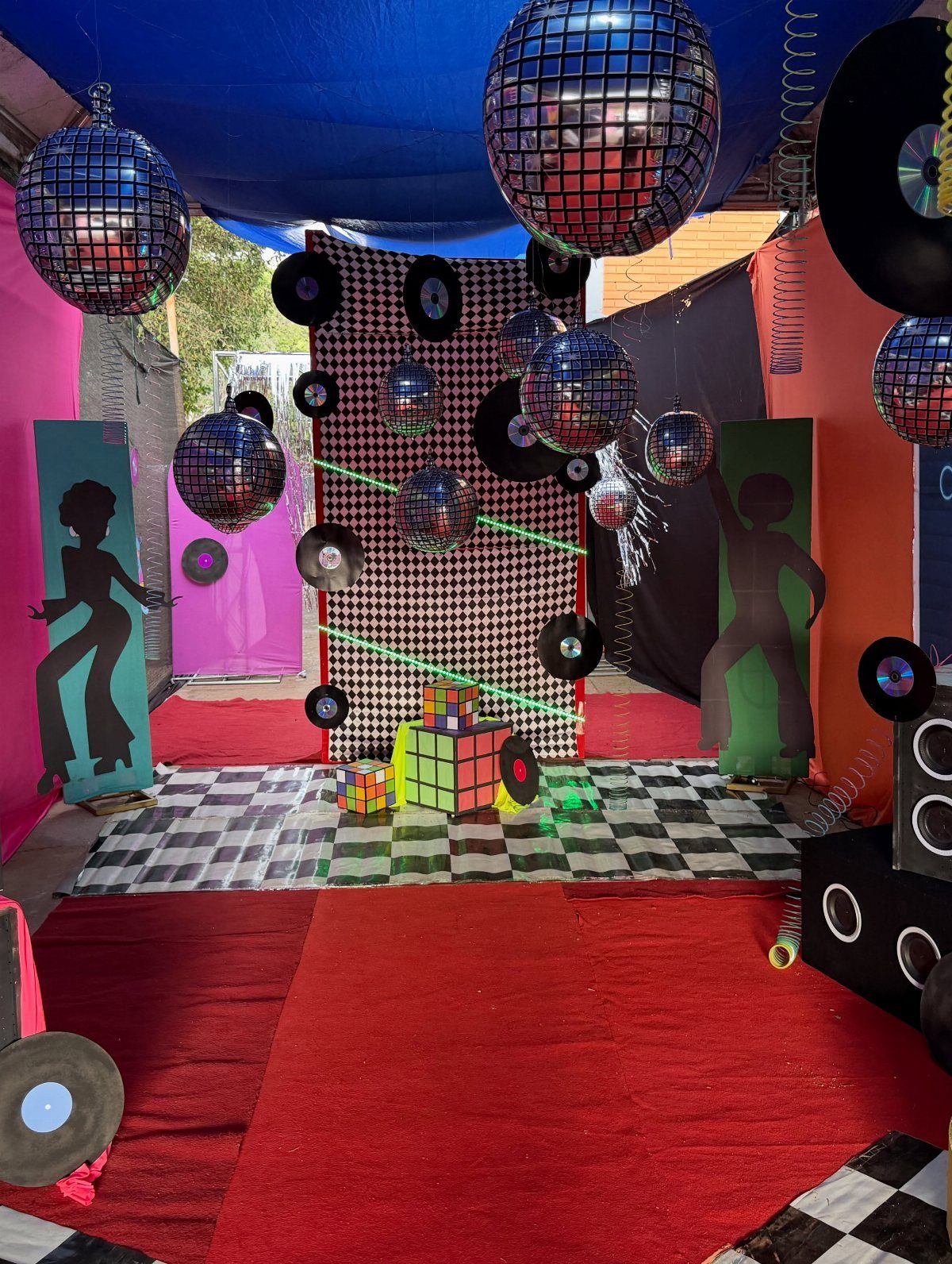 Party setup with disco balls, vinyl records, and dancing silhouettes on red carpet.