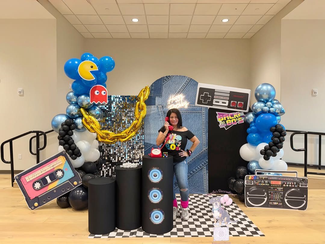Woman posing in an 80s themed photo booth with balloons and retro props.