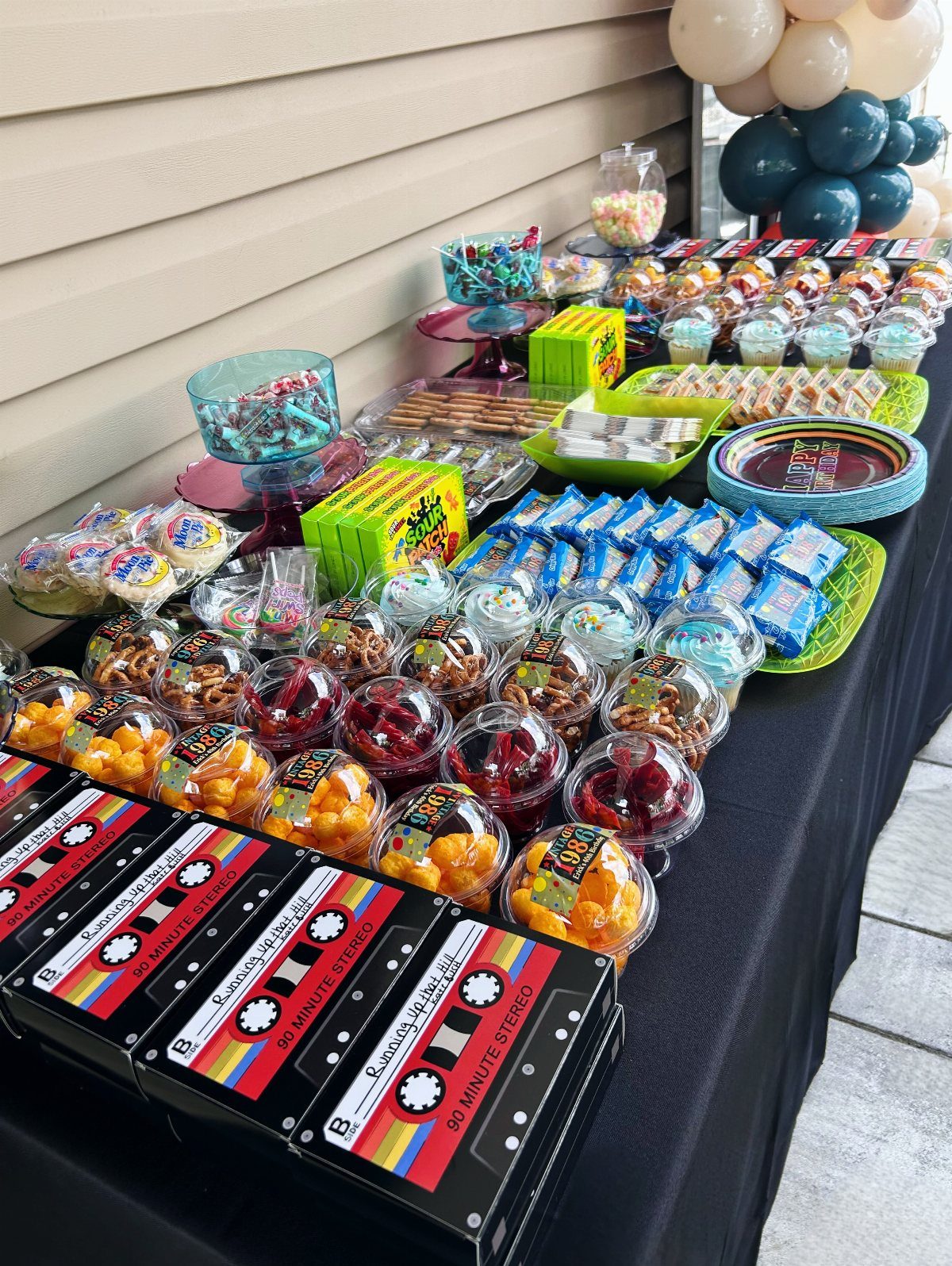 Candy bar with colorful sweets and cassette tape boxes on a black table.