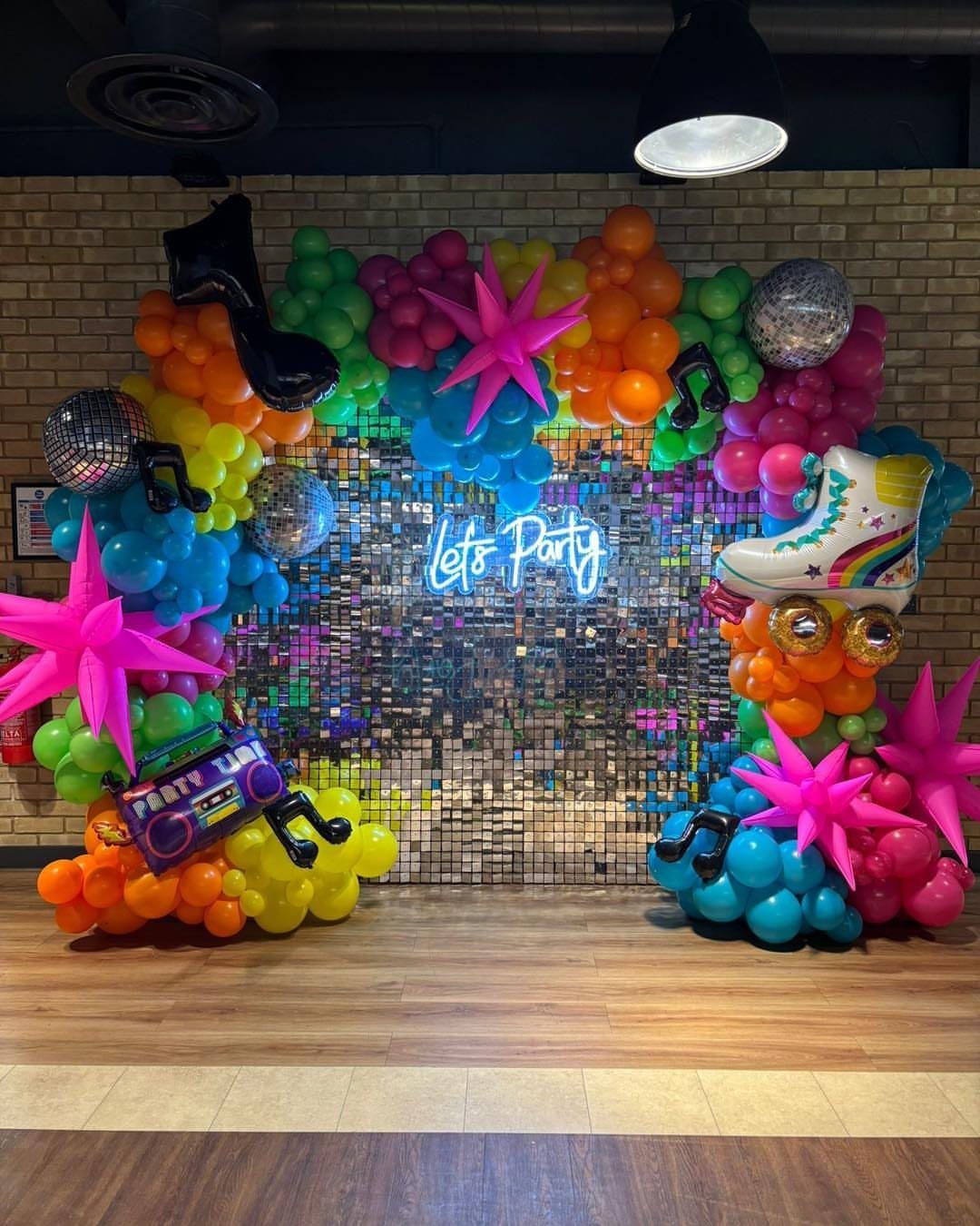 Colorful balloon arch with neon sign and disco balls against a sequin wall.