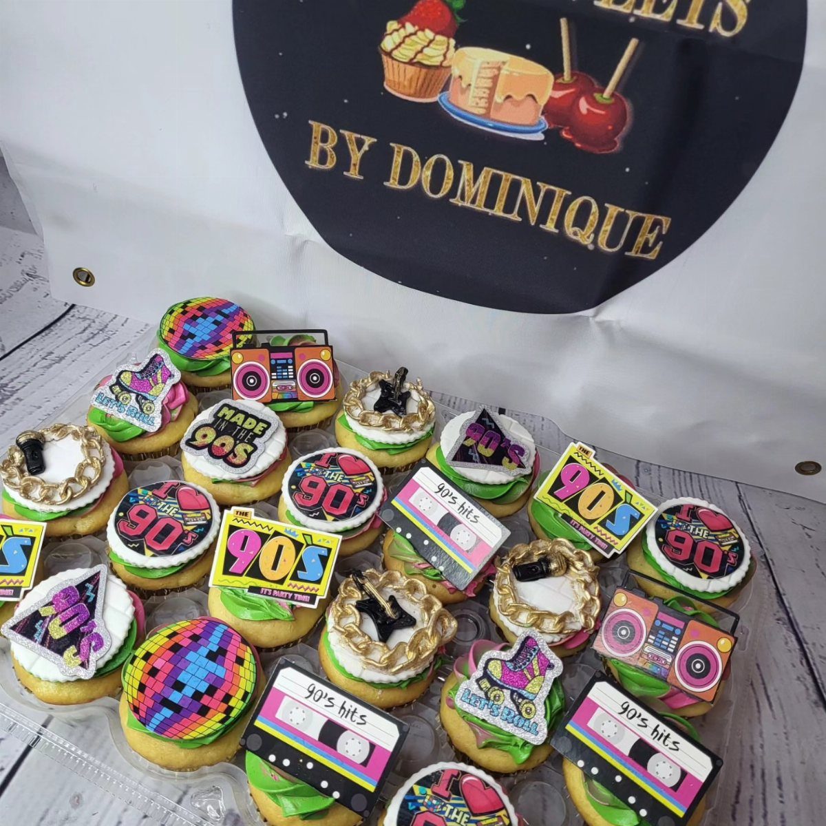 Cupcakes with 90s themed edible toppers like boomboxes and cassette tapes in a container.