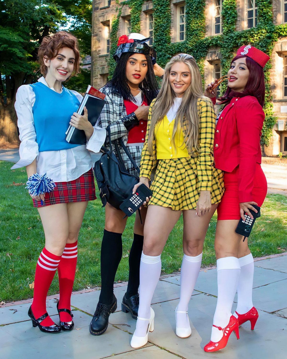 Four women in colorful 90s schoolgirl costumes posing outdoors with vintage mobile phones.