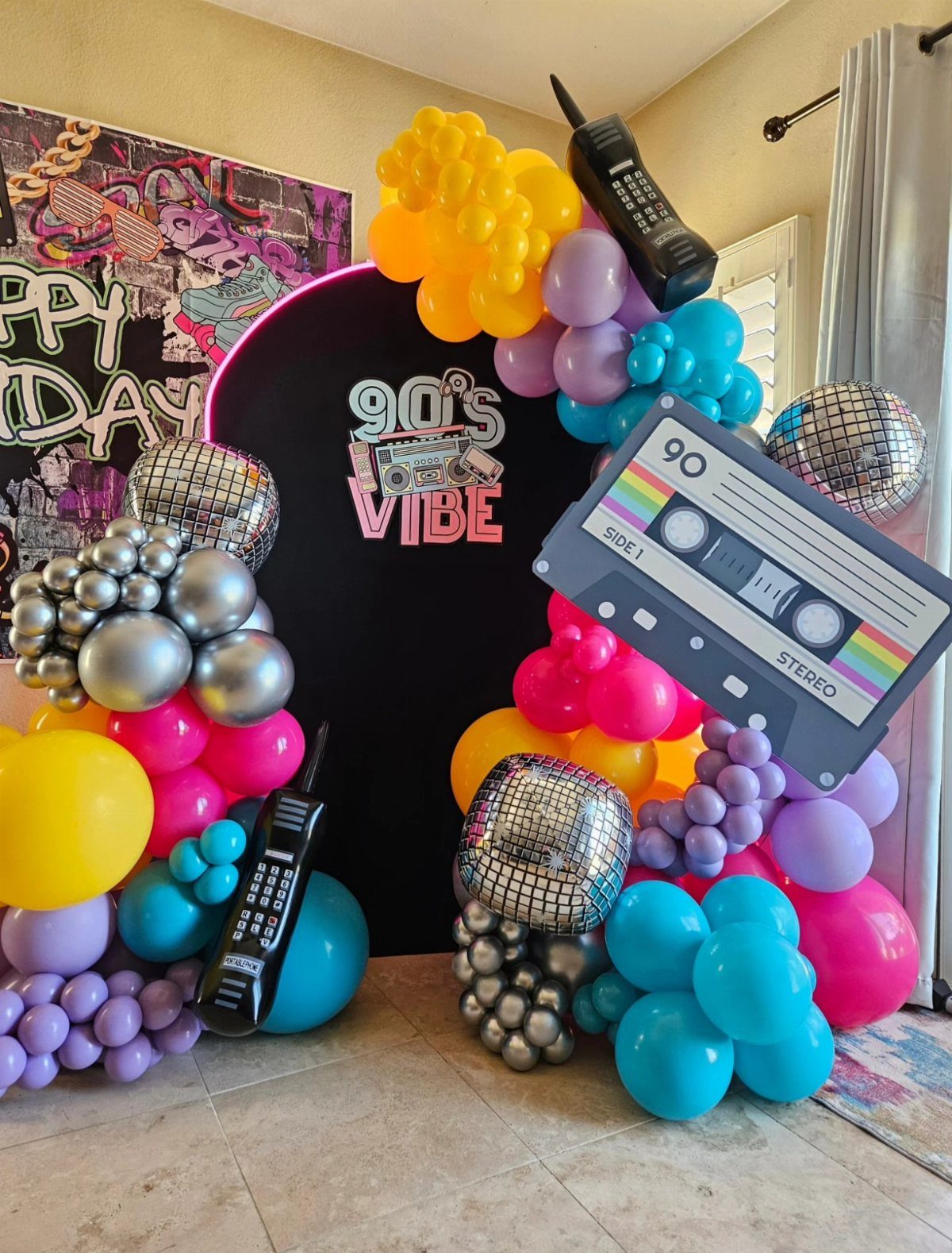 90s themed party backdrop with colorful balloons, disco balls, and cassette tape cutout