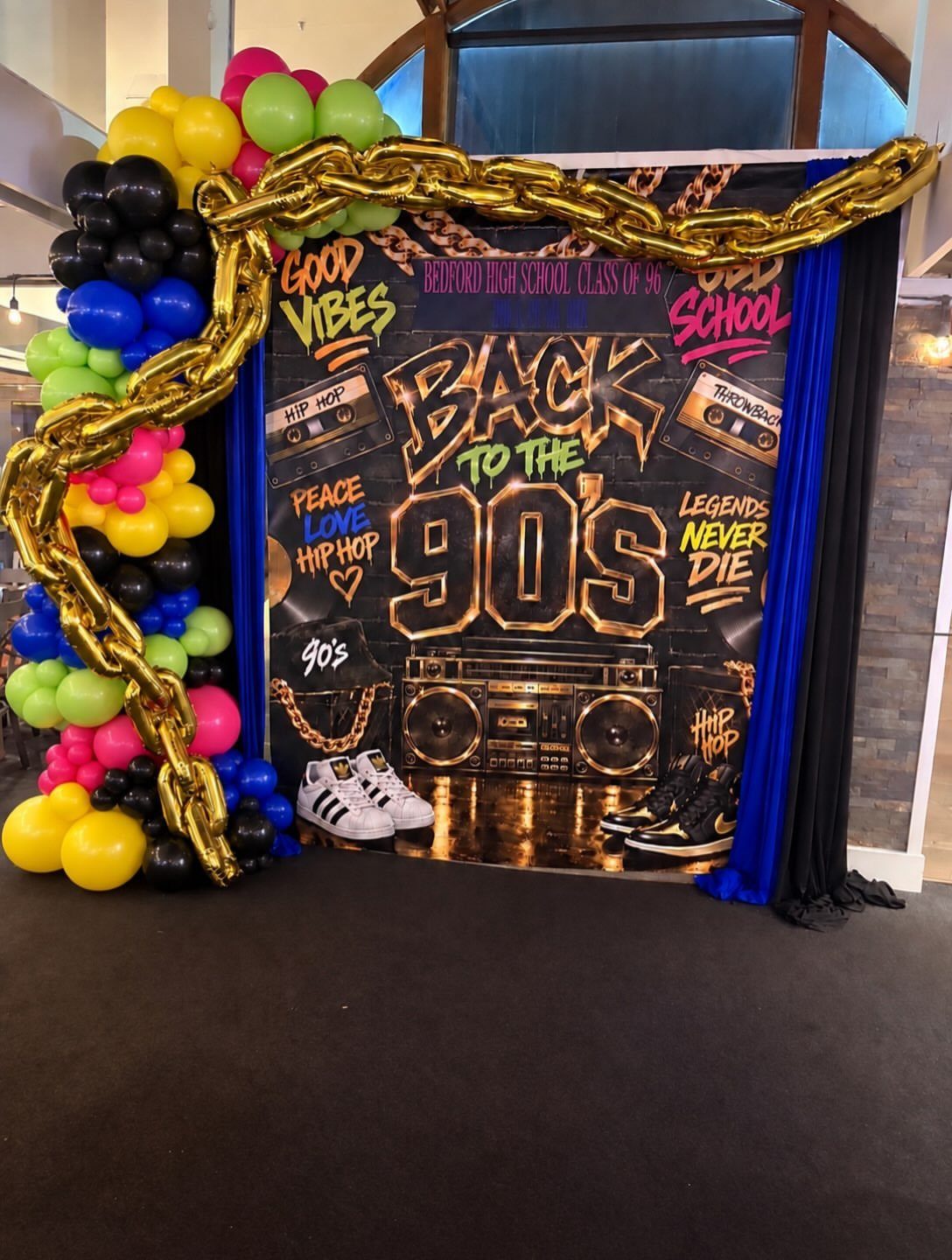 90s themed photo booth backdrop with colorful balloons and gold chain decorations