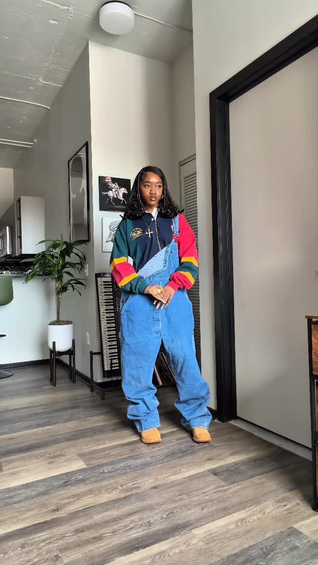 Woman wearing oversized denim overalls and a colorful striped sweater in a room