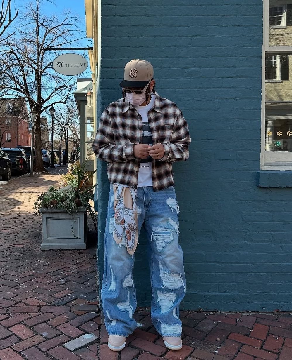 Person wearing a plaid flannel shirt and baggy distressed jeans against a blue wall