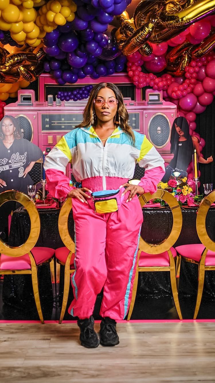 Woman in neon 90s tracksuit posing before colorful balloons and boombox backdrop