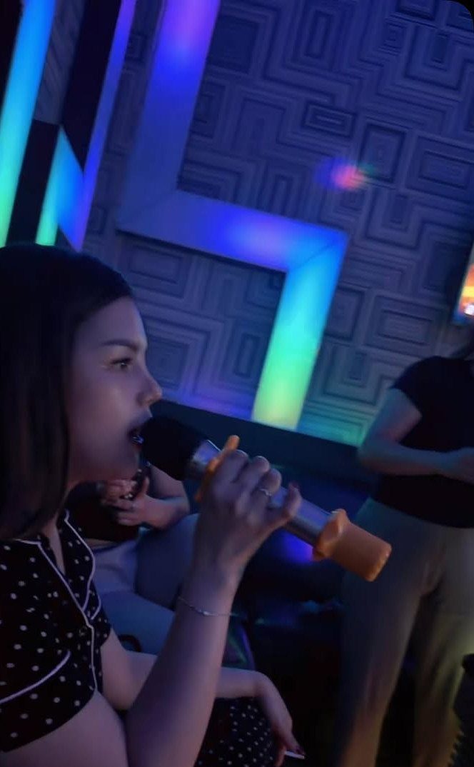 Woman singing into a microphone in a room with neon geometric lights.
