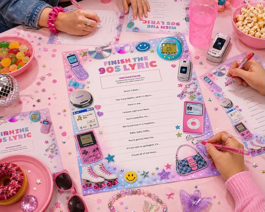Hands writing on 90s lyric game sheets surrounded by nostalgic pink accessories
