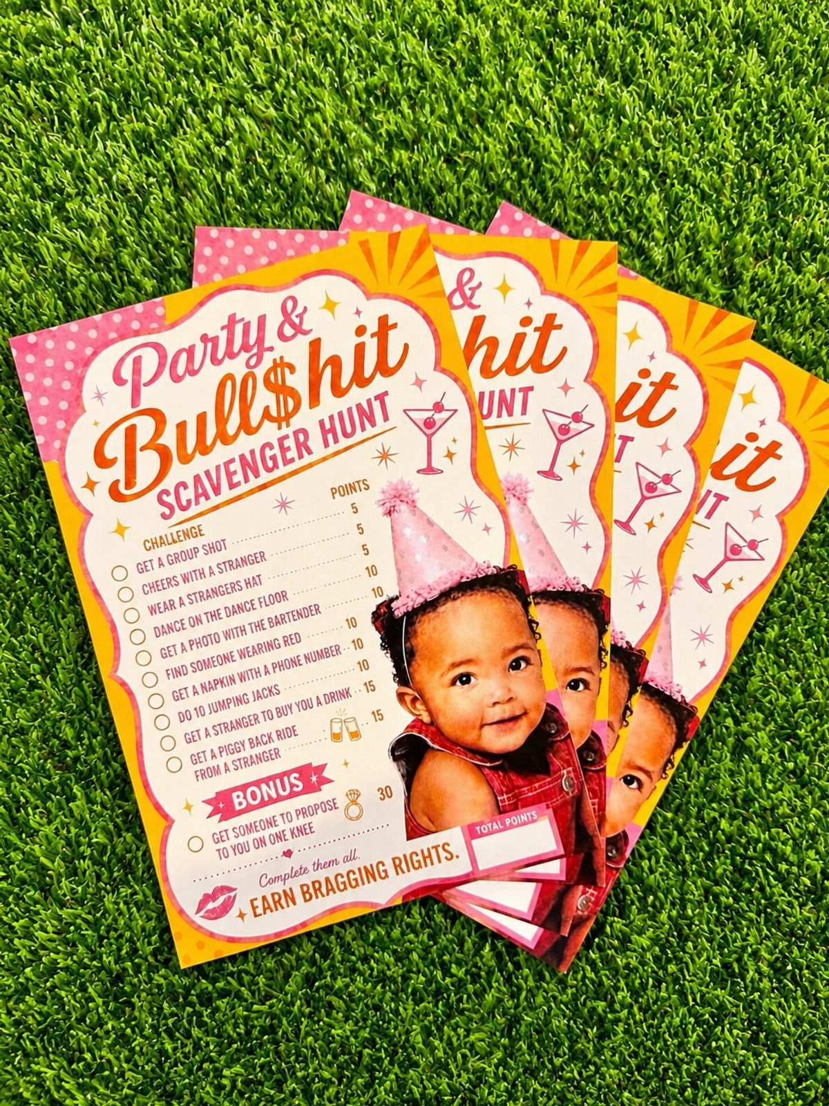 Scavenger hunt game cards with a baby's photo resting on green artificial grass.