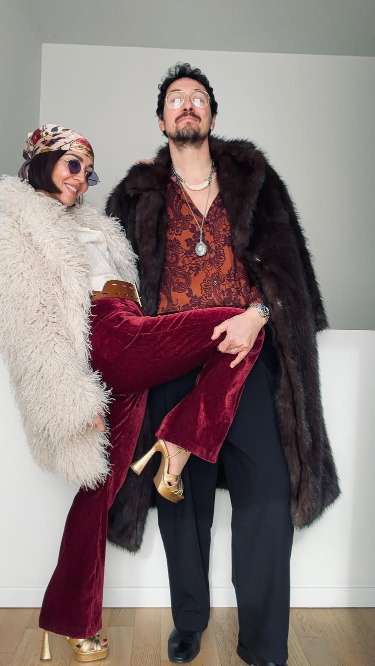 Man and woman posing in 1970s disco outfits with faux-fur coats and velvet flares.