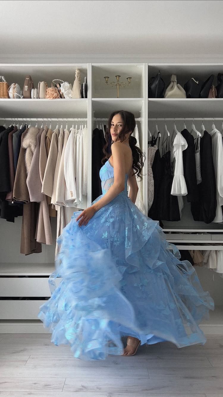 Woman in a voluminous light blue ruffled ballgown posing in a white closet