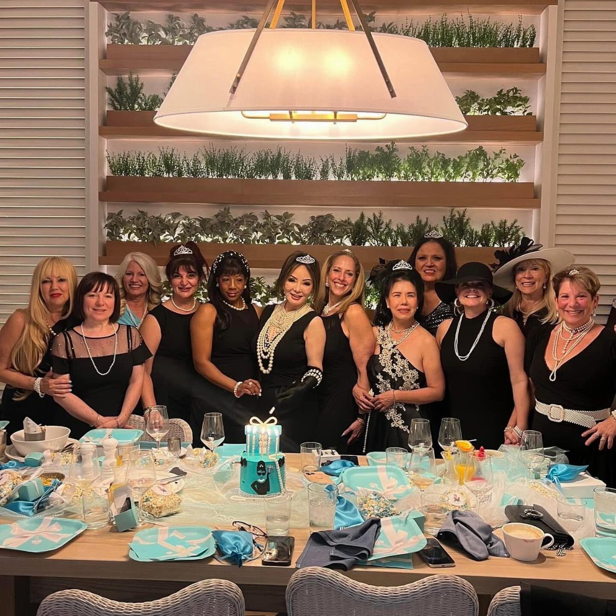 Women in black dresses and pearls posing behind a Tiffany blue themed table.
