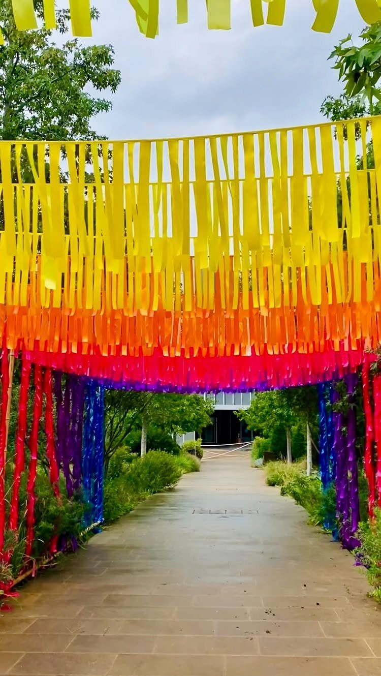 Rainbow fabric strips hanging as a canopy over a stone garden pathway.