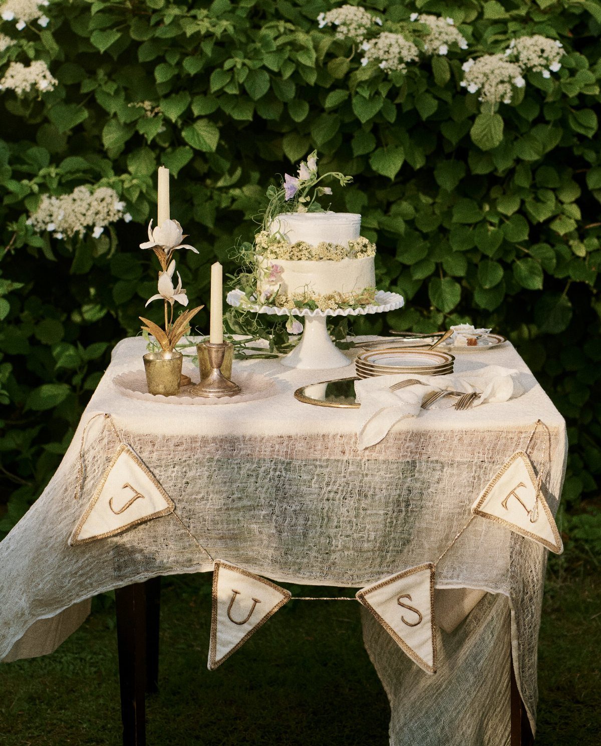 White tiered wedding cake on a lace-covered table with a JUST bunting banner.