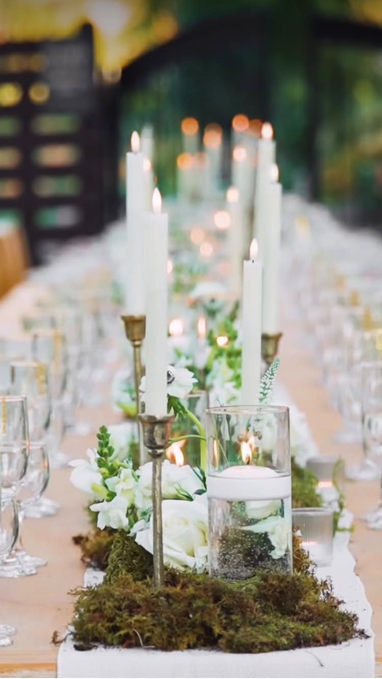 Green moss table runner with white flowers and white candles on a wooden table