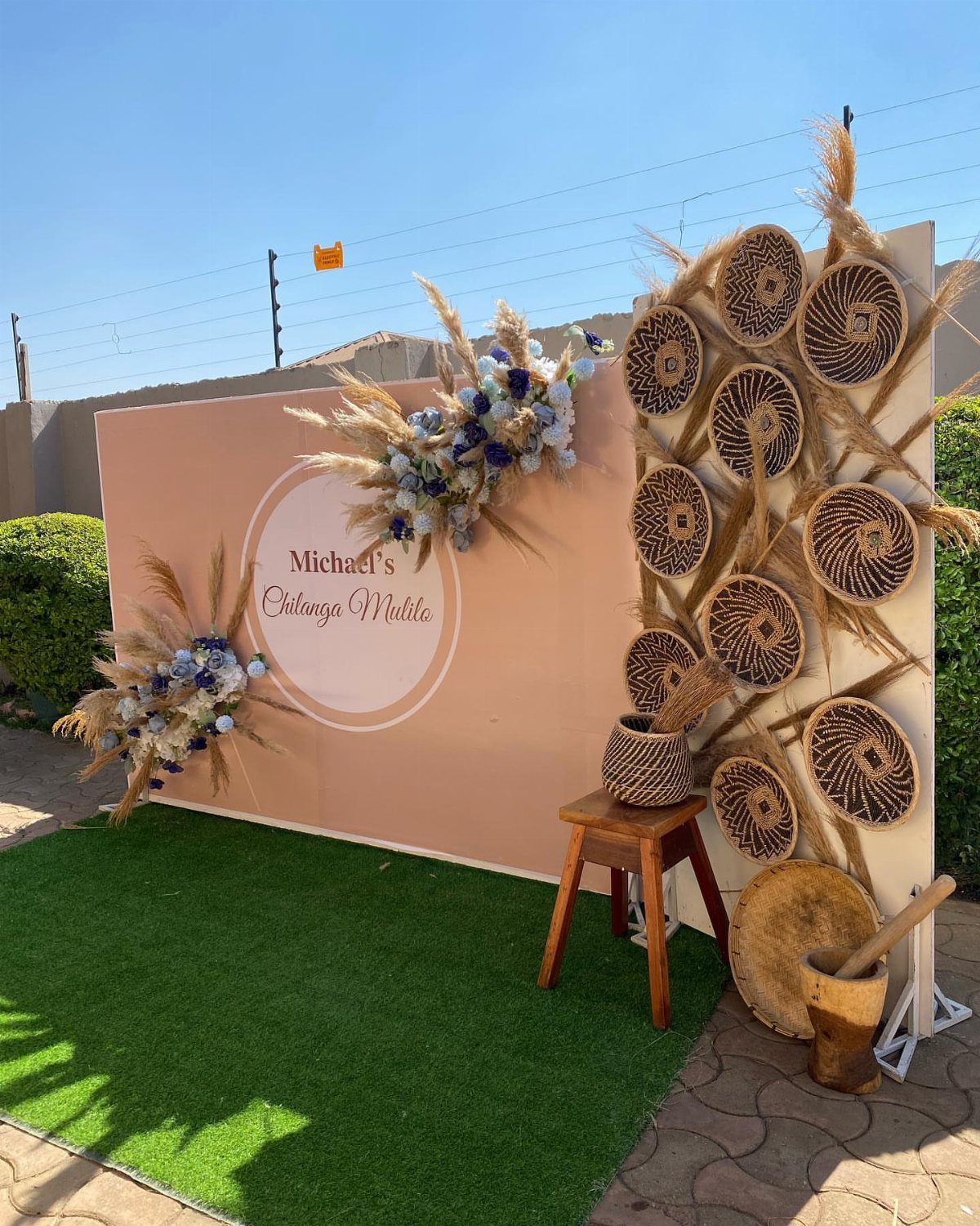 Peach backdrop with floral arrangements and woven baskets on a green turf lawn.